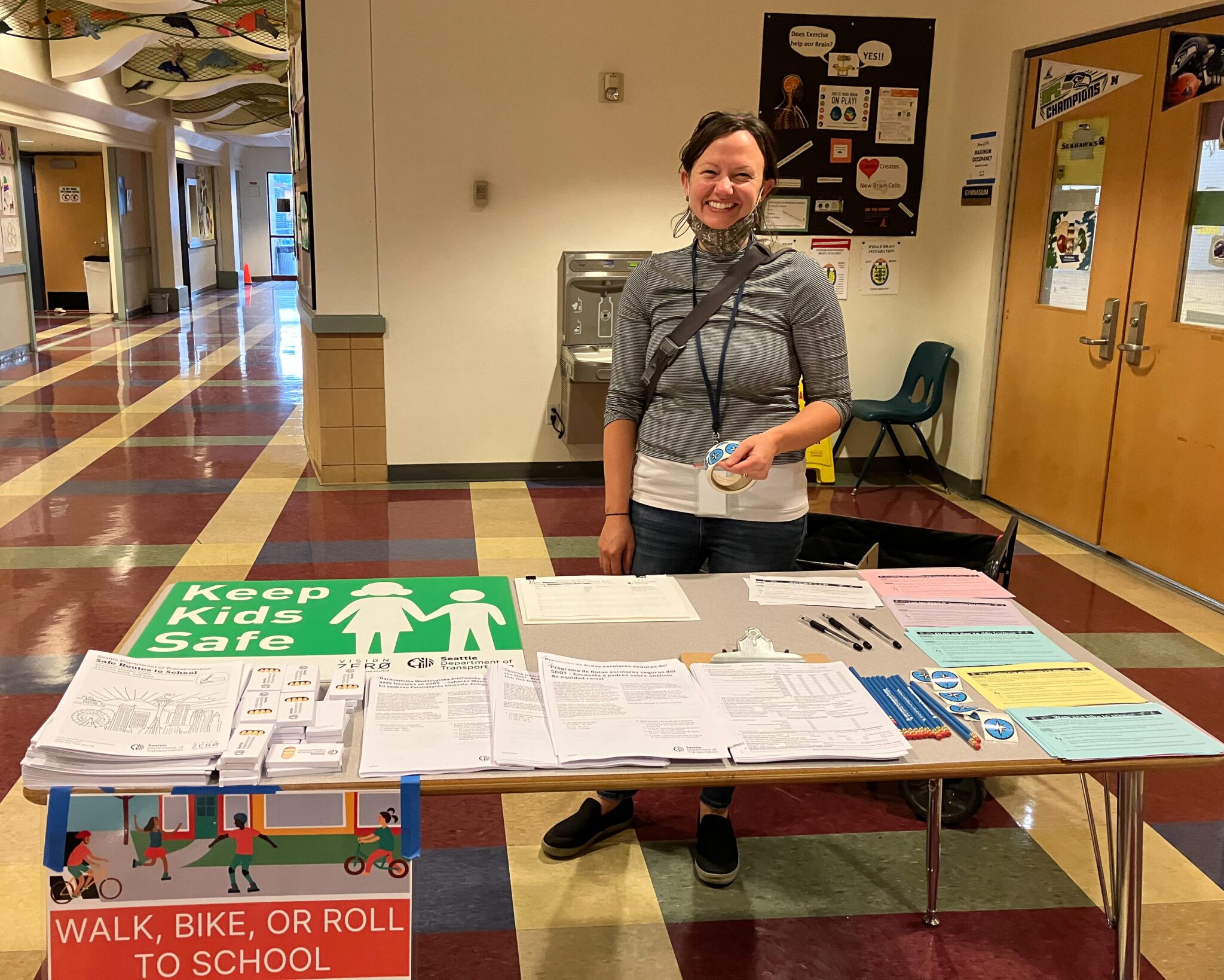 A woman smiles at the camera while standing in front of a table of informational handouts inside a building.