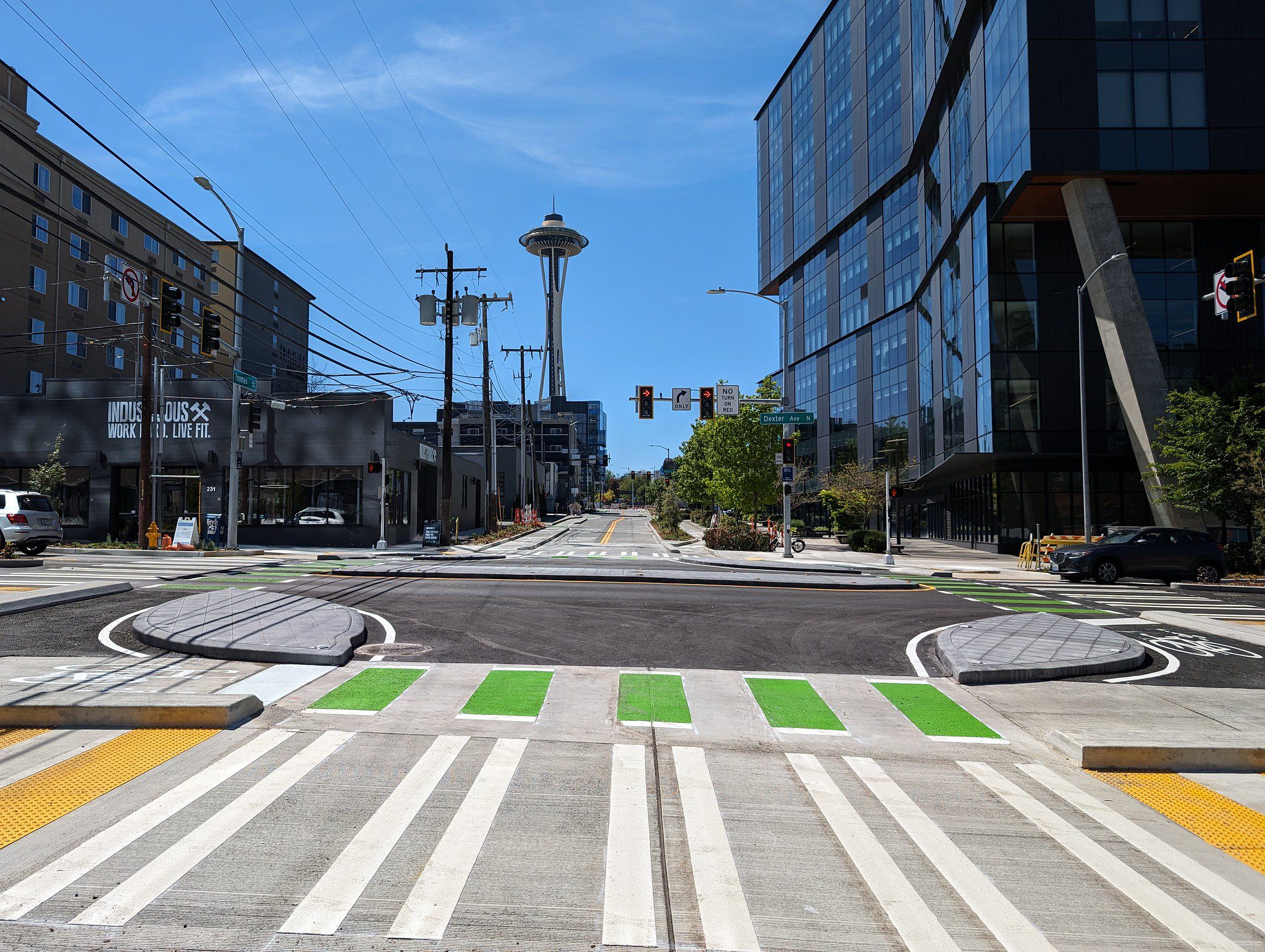View of a crosswalk and bike path next to a street and large buildings with the Space Needle in the background.