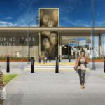 A gray building represents a future light rail station. The building has a tower in the middle with images of people's faces. Blue sky with clouds. Bollards on the sidewalk separate sidewalk from the street. Three people walking by on the sidewalk. Image has a computer-generated rendering appearance.