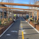 Two people work on landscaping near a bike lane on a sunny day outdoors.