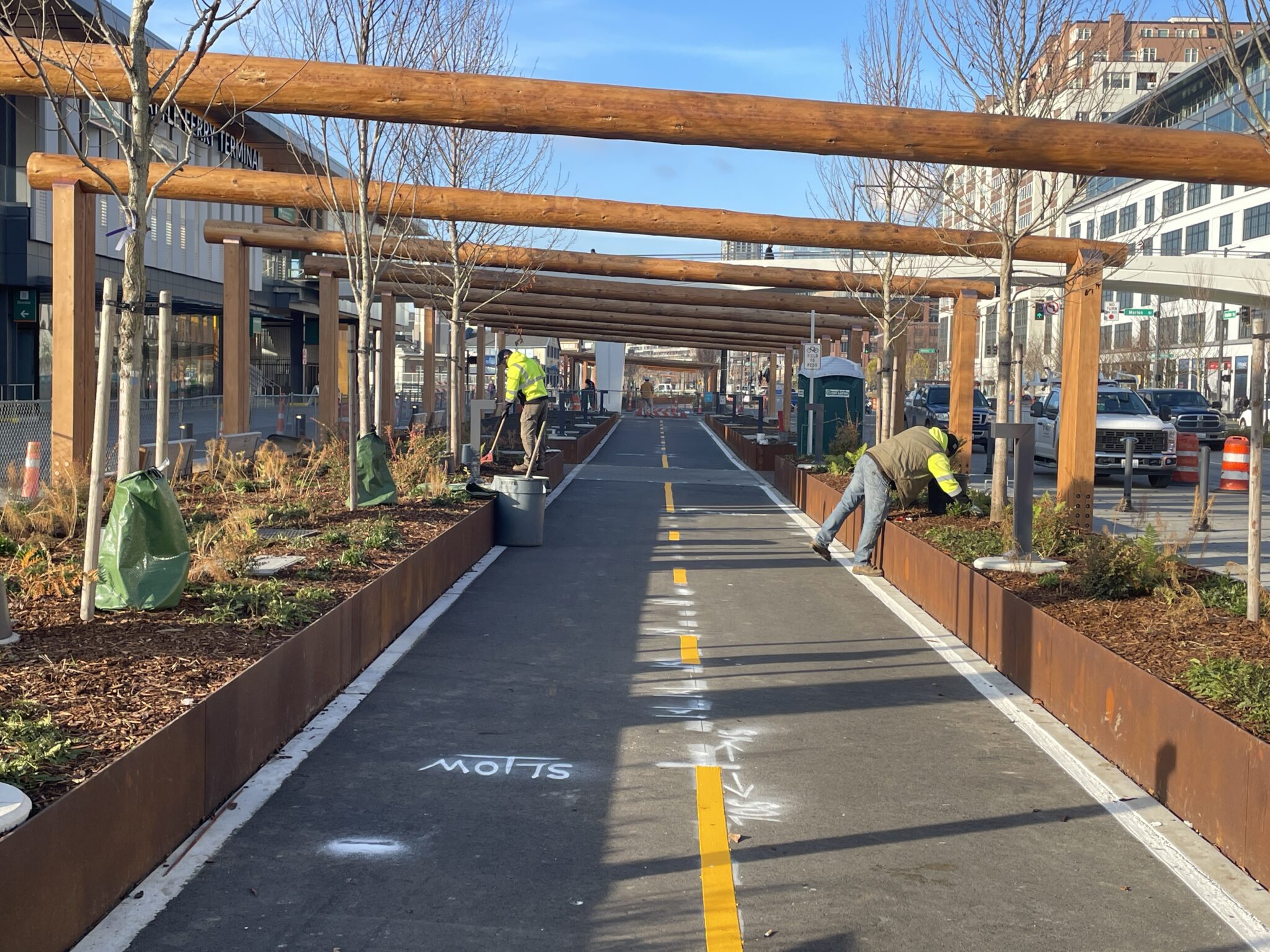 Two people work on landscaping near a bike lane on a sunny day outdoors.