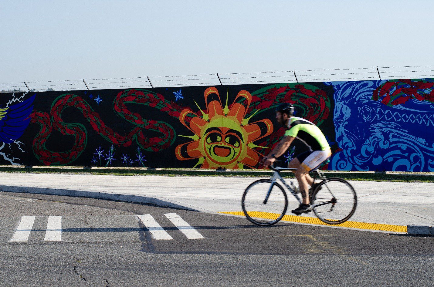 A person bikes into the street at a marked crosswalk with a large colorful mural in the background.