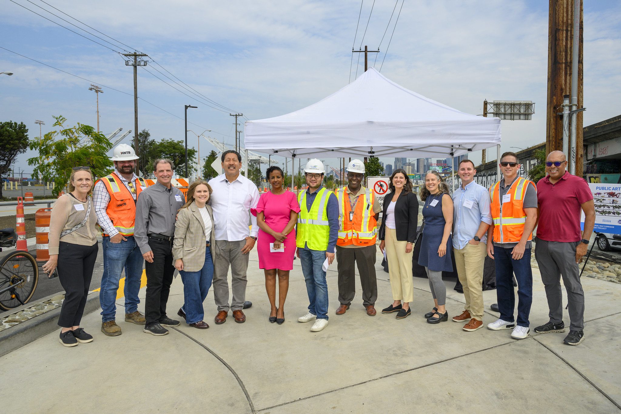 A large group of people smile while looking at the camera on a partly sunny, partly cloudy day. A white canopy tent is in the background.