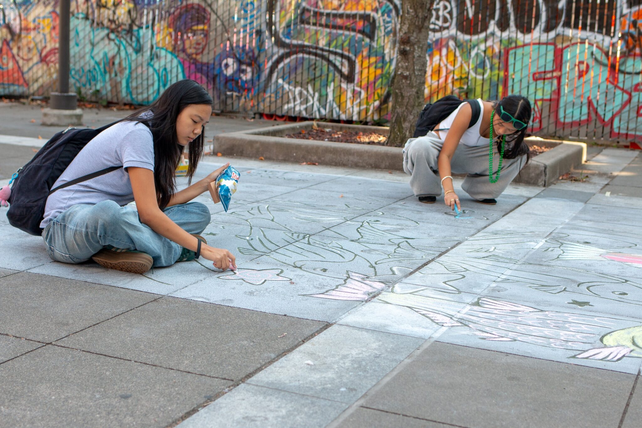 Two people create artwork on a large public plaza area on a clear, sunny day.