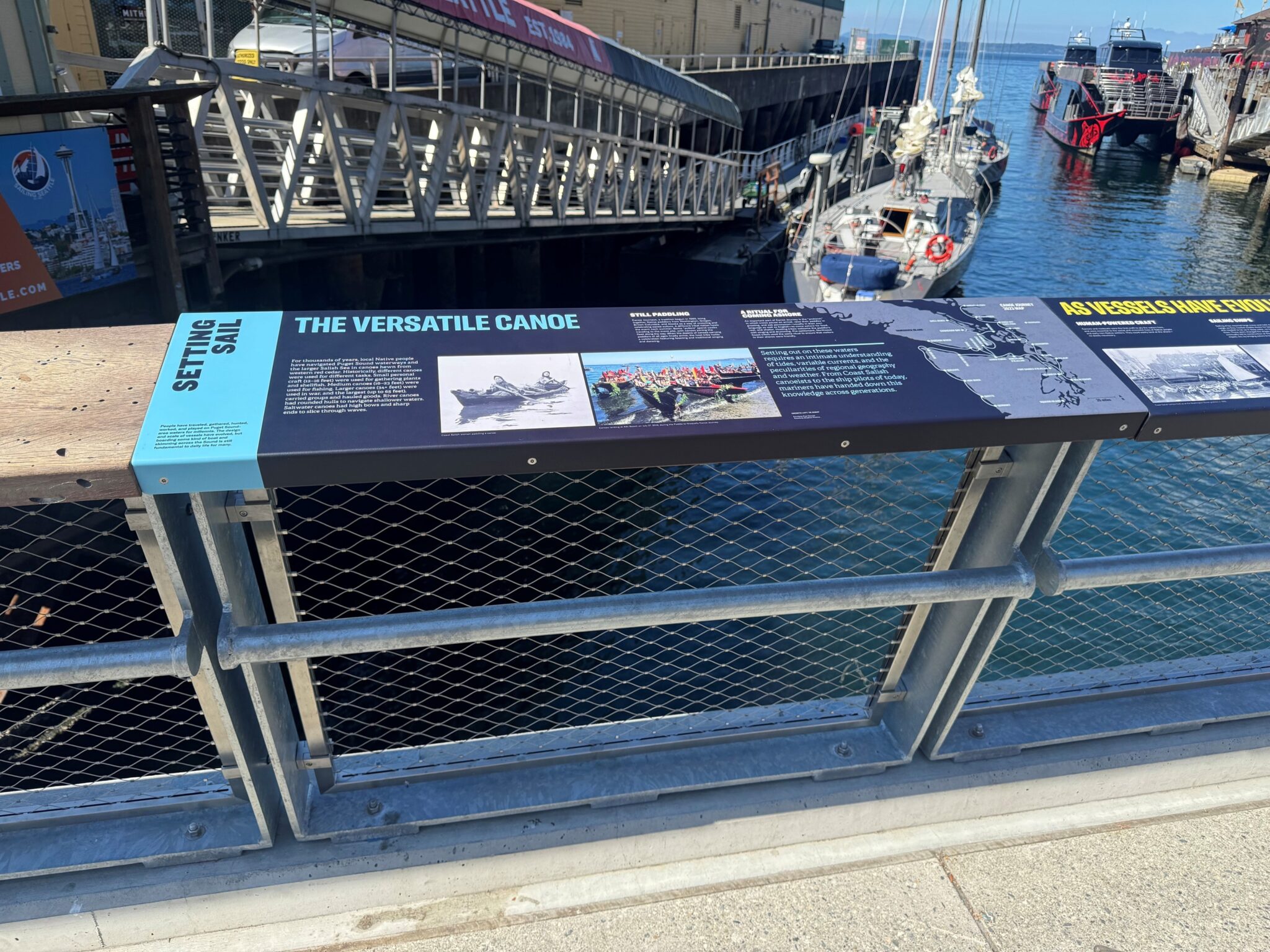 A photo of an interpretive sign with boats and water and a dock below.