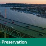 Aerial photo of a large bridge in the evening, with water in the background. The image includes the worlds "Revive I-5 Ship Canal Bridge Preservation" and the WSDOT logo.