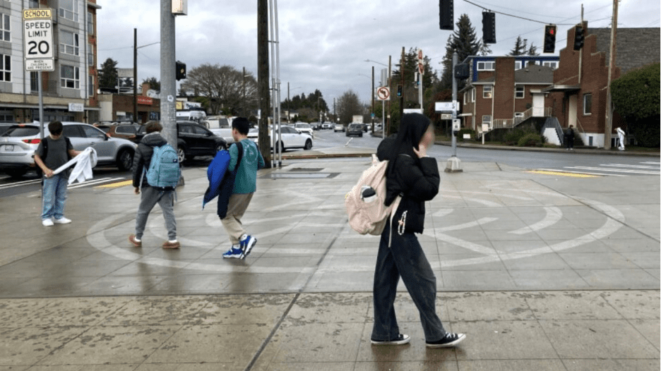 Four students walk in a plaza on a rainy day. Two of the students are walking inside a labyrinth on the ground.