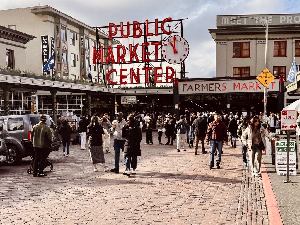 A bustling street scene at Pike Place Market in Seattle features the iconic red 