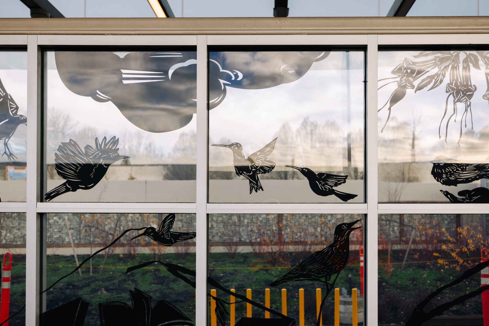 Glass windows featuring artwork fill the frame. The artwork contains black silhouettes of birds and plants.