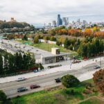 Ariel view of Judkins Park light rail station in Seattle. In the distance, a freeway, fall-colored trees, and a cityscape are visible.
