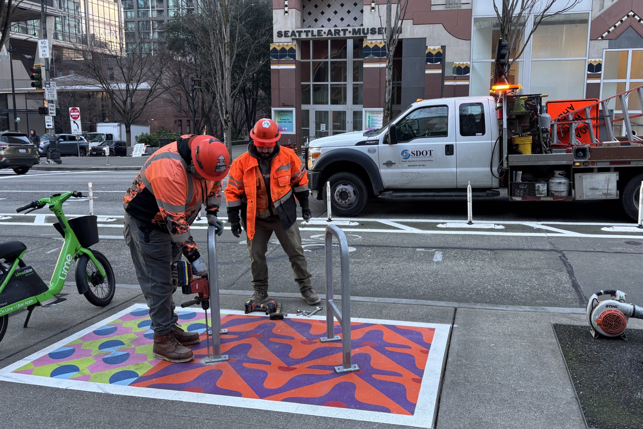 Two SDOT workers install bike racks on a colorfully painted corral in front of the Seattle Art Museum.