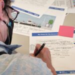 A person with glasses and a black face mask is writing on a feedback form. The table is covered with planning documents. Logos for SDOT and King County Metro are visible on the bottom of the form. The top of the form says "My Vision for the Aurora Corridor".