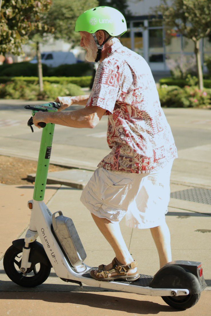 A man in a colorful shirt riding a lime scooter during a safety demonstration.