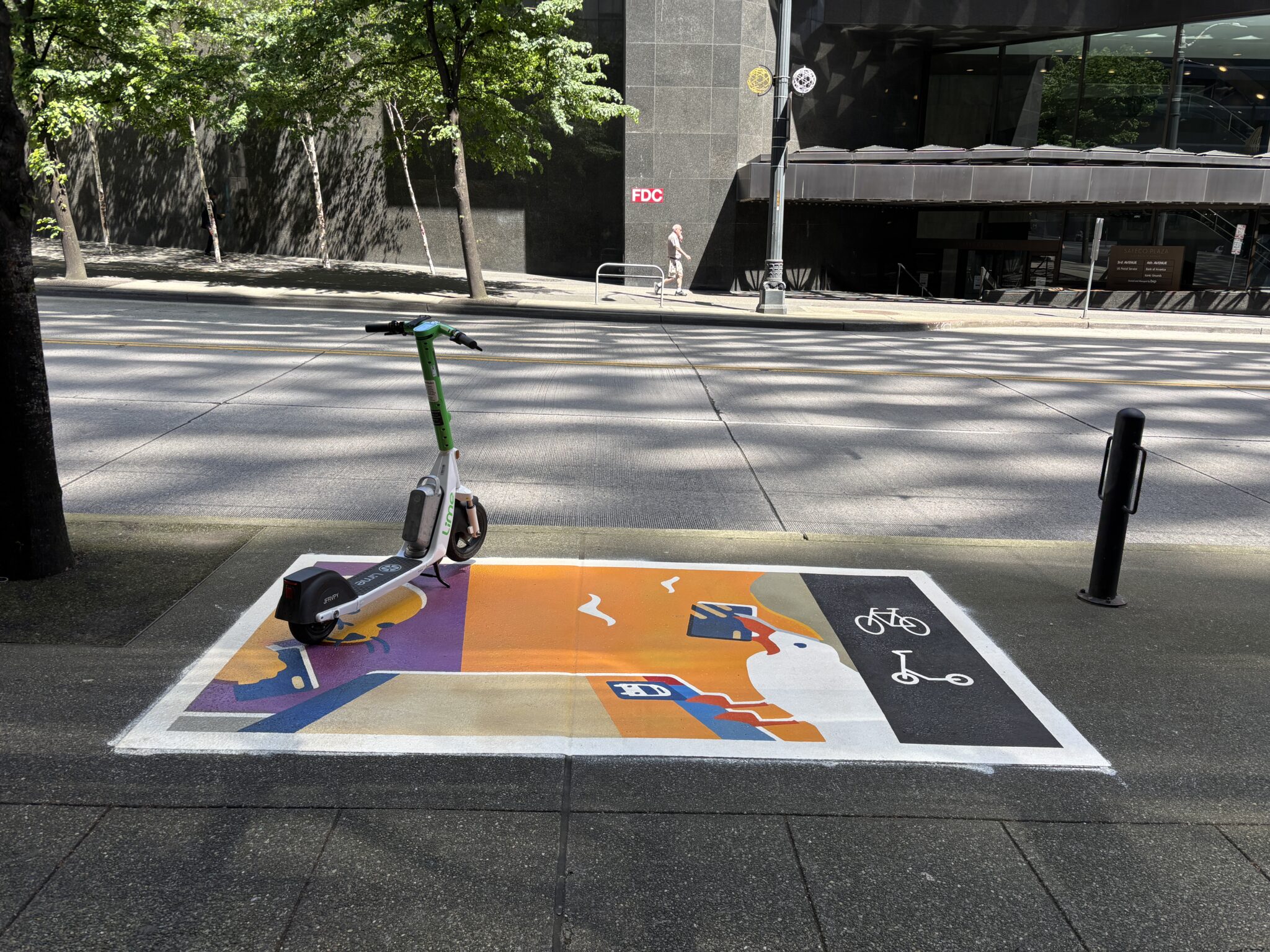 A white-and-green shared scooter is parked on a colorful sidewalk mural marked for bike and scooter parking. The mural uses bright orange, purple, blue, yellow, black, and white, and shows a large white bird with an orange beak holding a blue object, with smaller white bird shapes above it. A city street and tall office building are in the background, with tree shadows stretching across the ground.