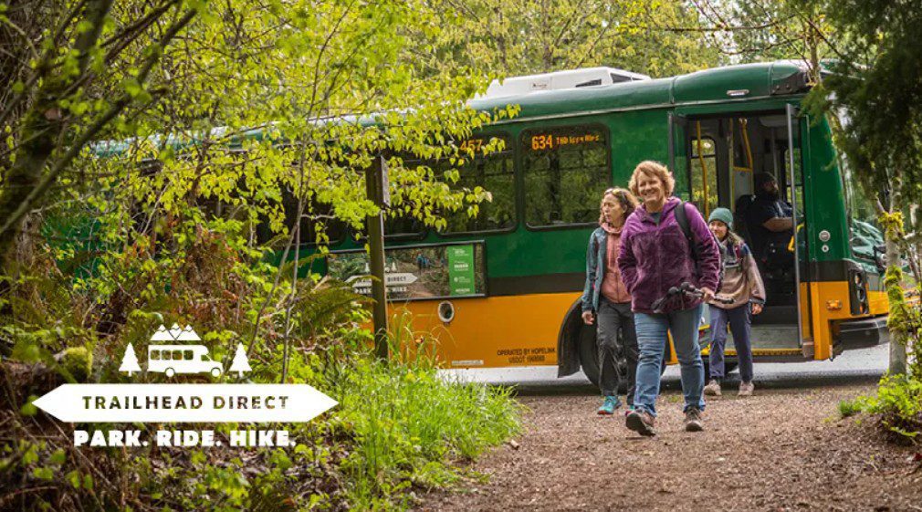 Three people walk off of a bus and start a hike in nature.