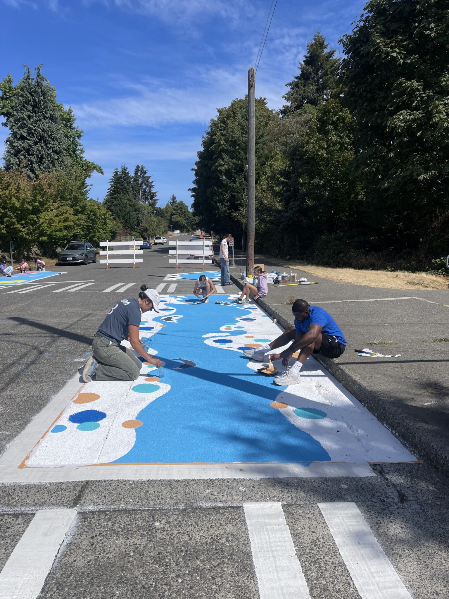 A group of people paint a large colorful mural on the street.
