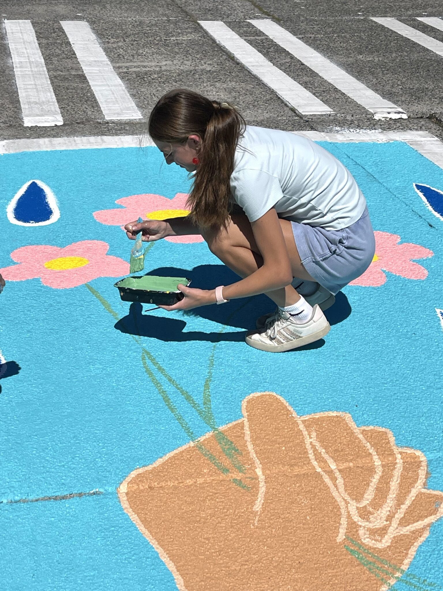 A person paints a large colorful mural on the street.