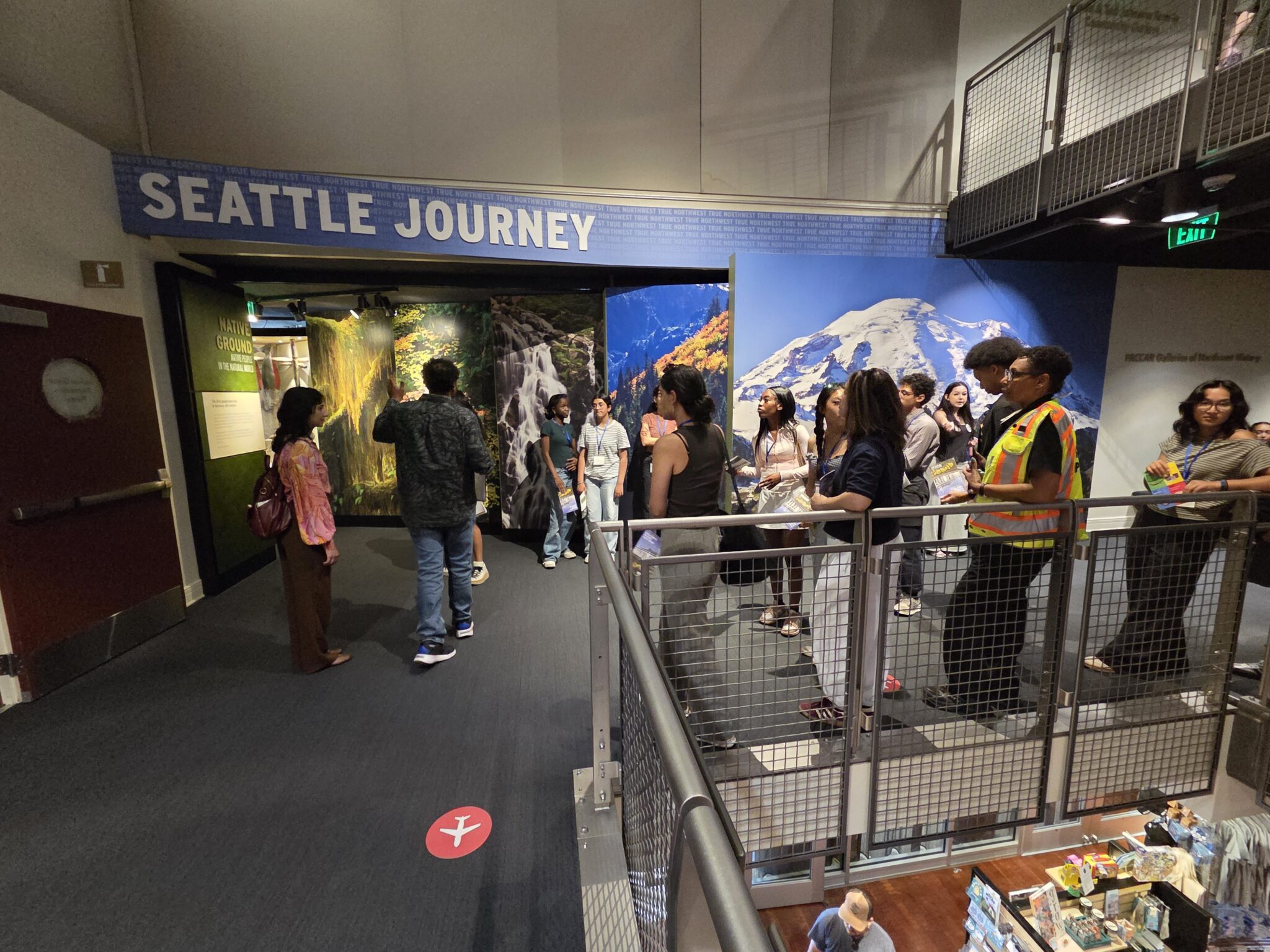 A group of people walk through a museum. The words "Seattle Journey" are in the middle of the image in large white lettering.