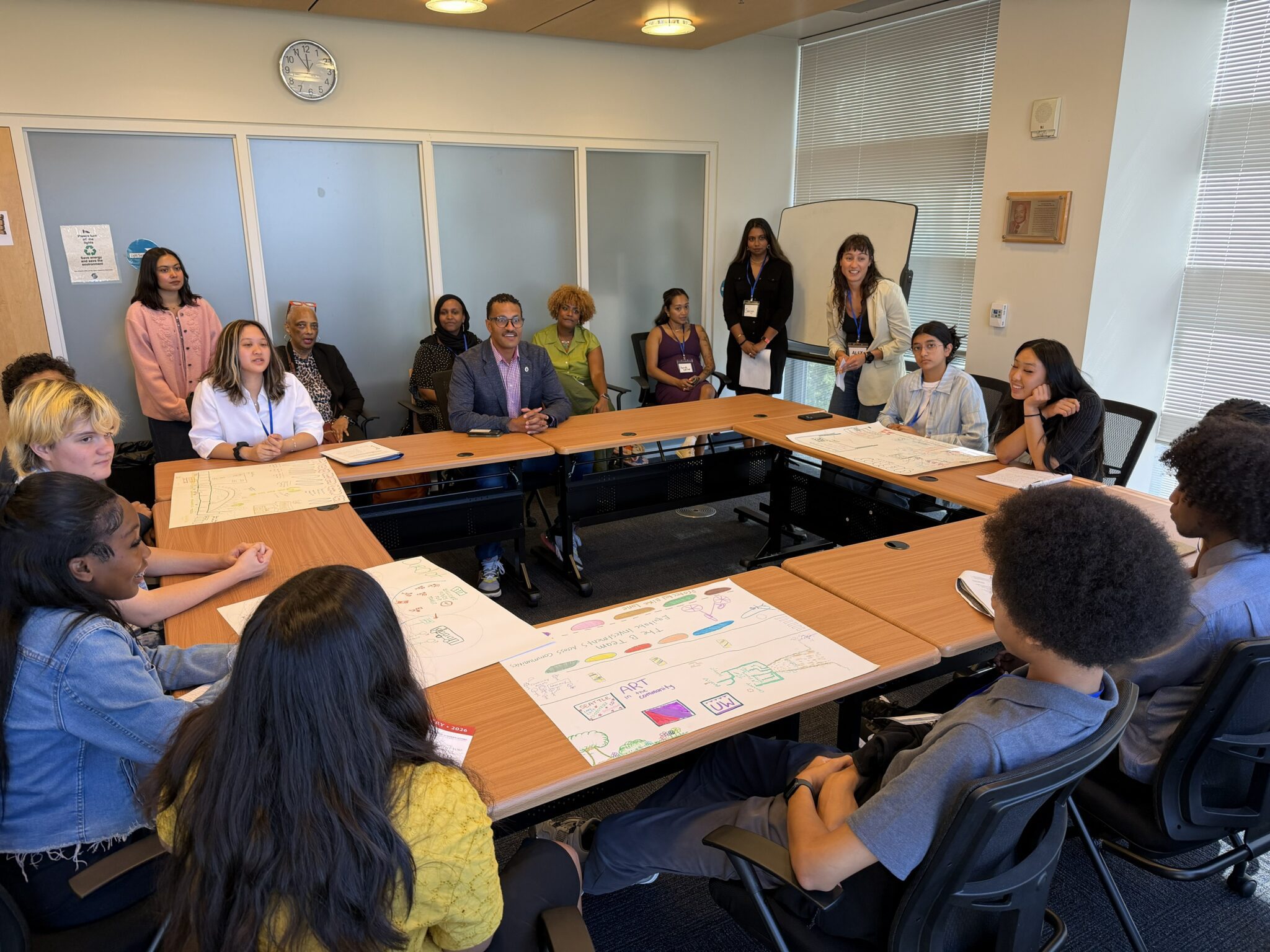 A group of people sit at a large round table inside a conference room while having a lively discussion.
