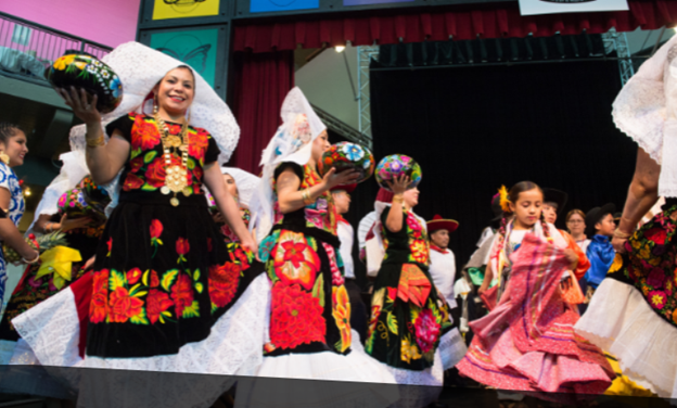 People dance wearing bright, colorful outfits at an indoor event.